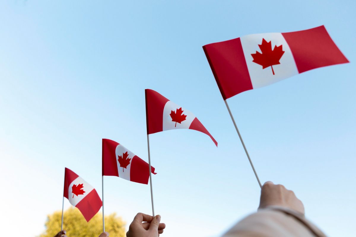 Hands Holding Canadian Flags Against Sky